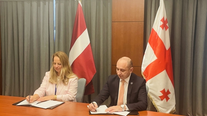 PTAC direktore Zaiga Liepiņa un Gruzijas Konkurences un patērētāju aģentūras pārstāvis paraksta sadarbības memorandu patērētāju tiesību aizsardzības un tirgus uzraudzības jomā. Fonā Latvijas un Gruzijas karogi