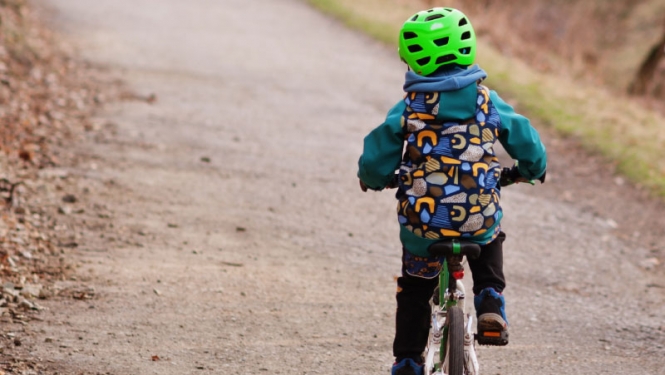 Bērns uz velosipēda, galvā koši zaļa aizsargķivere