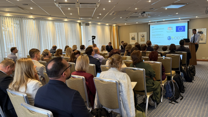 OECD sanāksme, konferenču zāle ar cilvēkiem, priekšā ekrāns