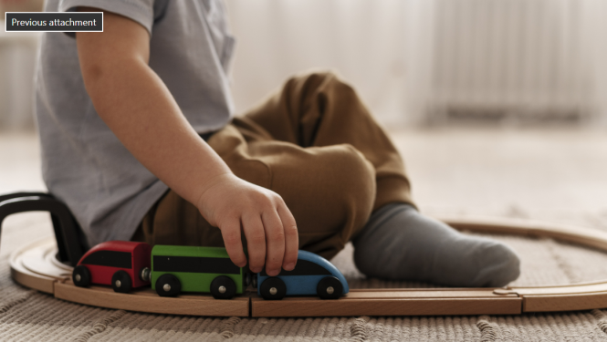 Zēns sēž uz grīdas un rotaļājas ar spēļu vilcieniņu, sliedes iet apkārt bērnam