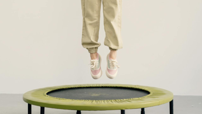 Meitene gaišā tērpā lēkā pa batutu