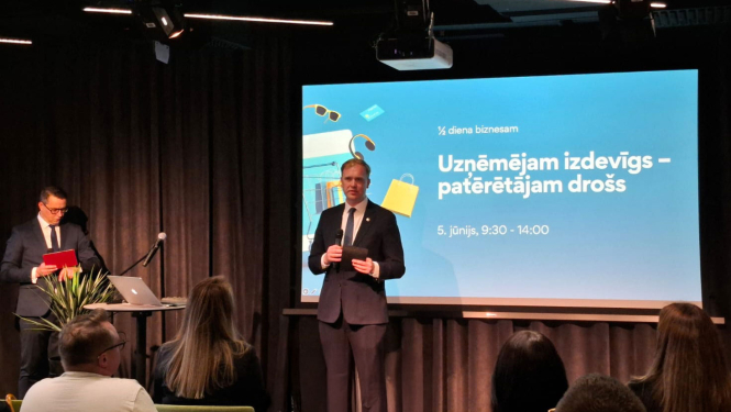 ViktorsValainis, ekonomikas ministrs, oie ekrāna ar uzrakstu - Uzņēmējam izdevīgs – patērētājam drošs