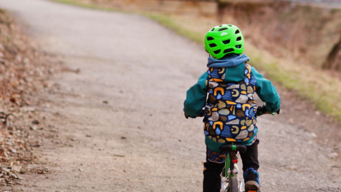 Bērns uz velosipēda, galvā koši zaļa aizsargķivere