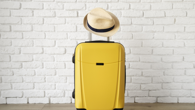 Dzeltens ceļotāja koferis un cepure uz kofera roktura