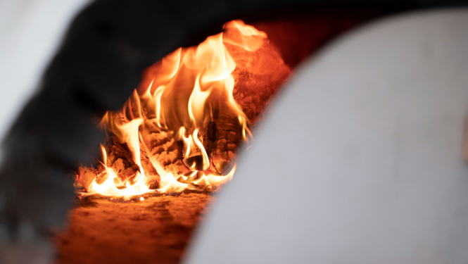 Krāsns ar kurināmo, krāsns durtiņas pavērtas, redzama uguns liesma