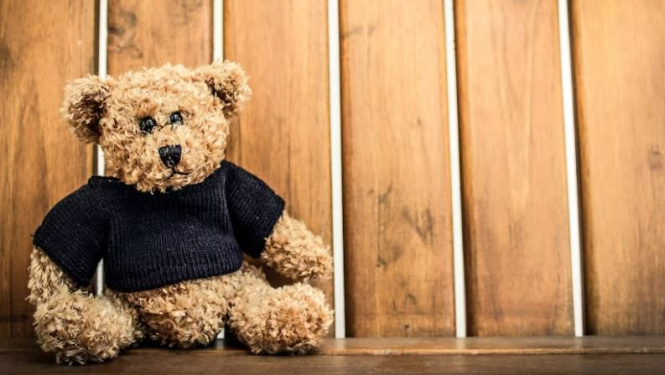 Rotaļu lācis pie brūnas koka sētas