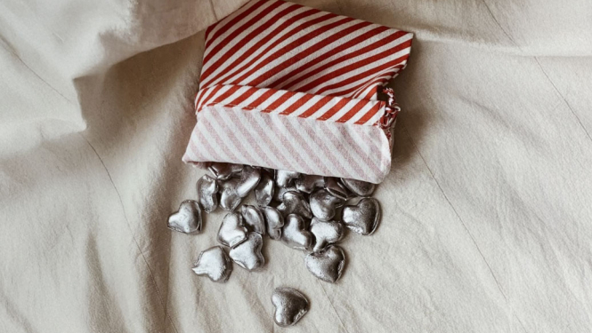 Vairākas svina laimītes sirds formā izbirušas no maisiņa uz linam līdzīga pārklāja.