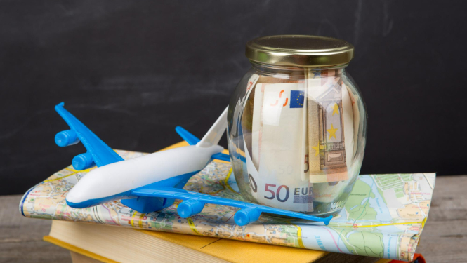 Spēļu lidmašīna uz salocītas pasaules kartes, virsū burka ar eiro naudas zīmēm