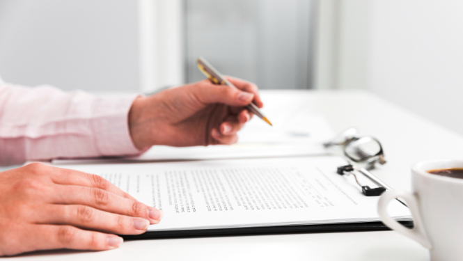 Uz galda līgums, roka ar pildspalvu, blakus kafijas krūze