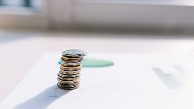 Monētu kaudzīte, uzlikta uz papīra lapas ar grafikiem.