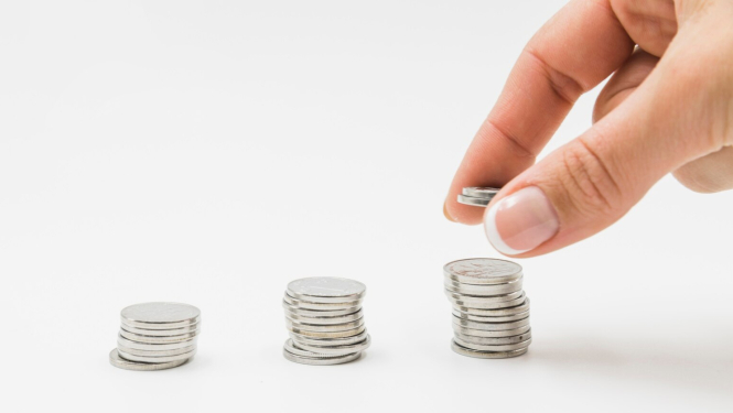 Trīs monētu kaudzītes, cilvēka pirksti pie vienas no kaudzītēm