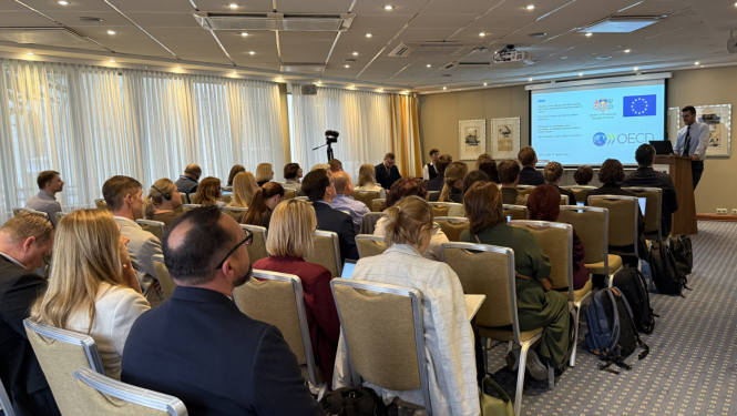 OECD sanāksme, konferenču zāle ar cilvēkiem, priekšā ekrāns