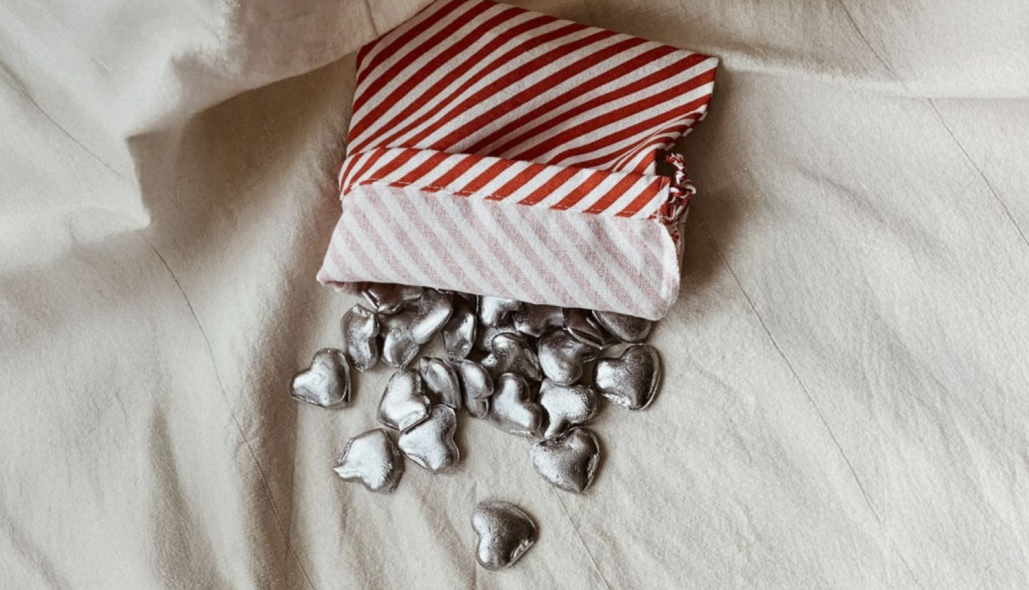 Vairākas svina laimītes sirds formā izbirušas no maisiņa uz linam līdzīga pārklāja.